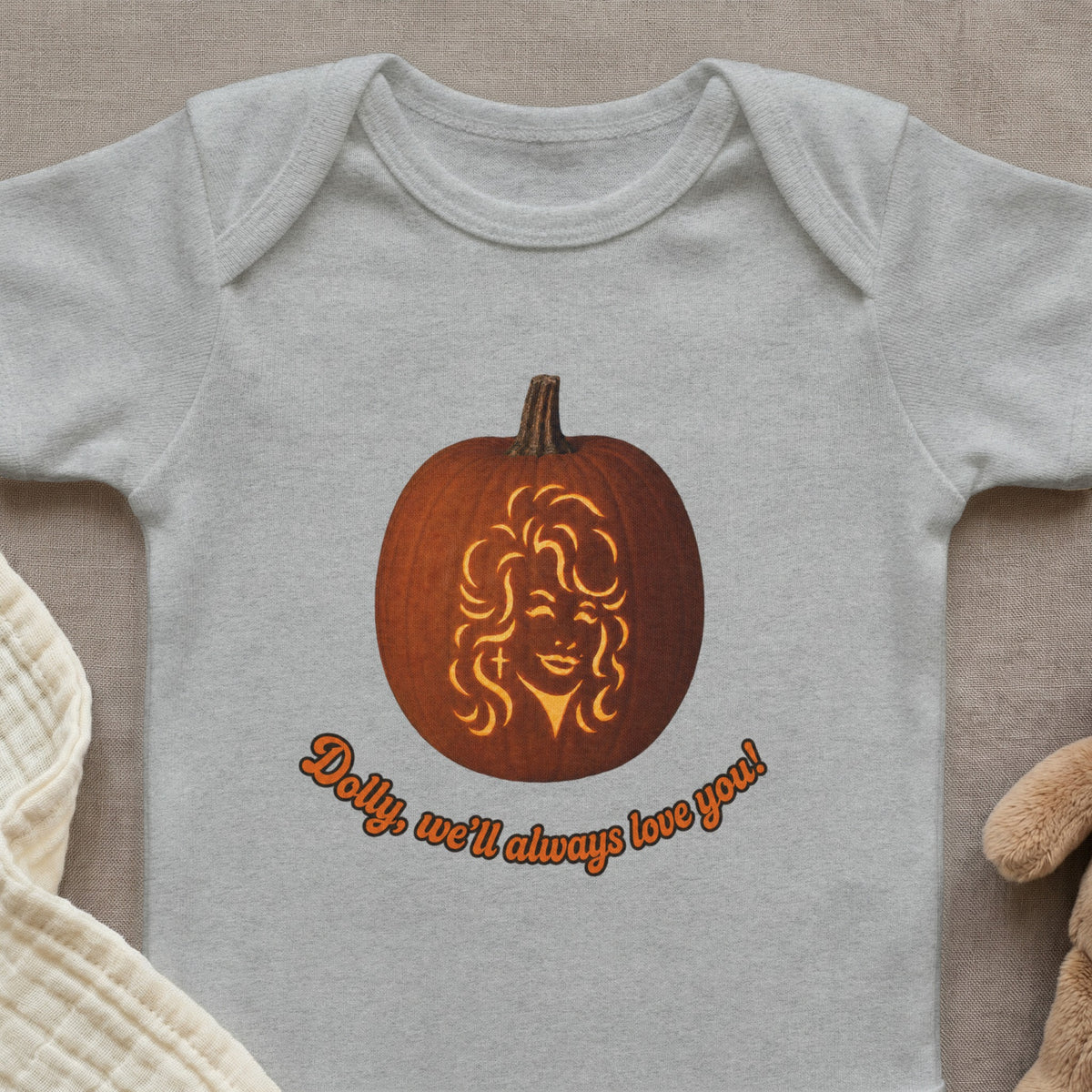 Baby bodysuit with a jack-o-lantern carved with Dolly Parton's face and orange text.
