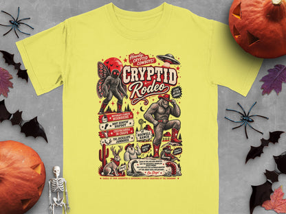 Yellow t-shirt with Cryptid Rodeo design featuring Bigfoot, Mothman, and other creatures.