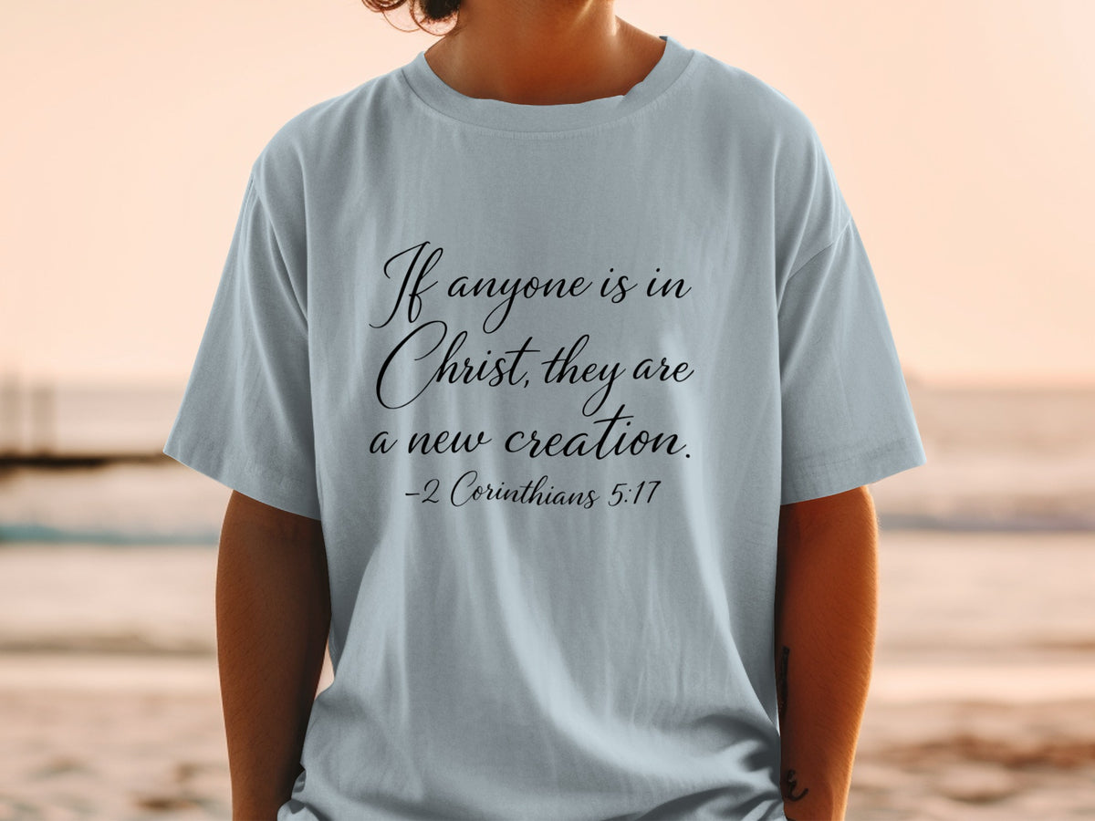 Light blue t-shirt with black cursive text: If anyone is in Christ, they are a new creation. -2 Corinthians 5:17