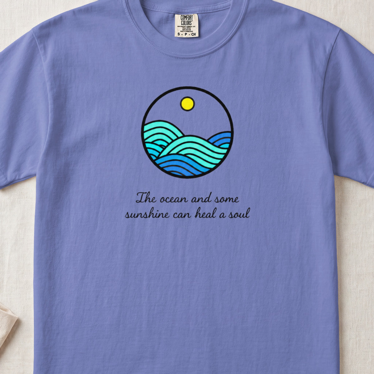 Purple t-shirt with a circular ocean and sun graphic and text.