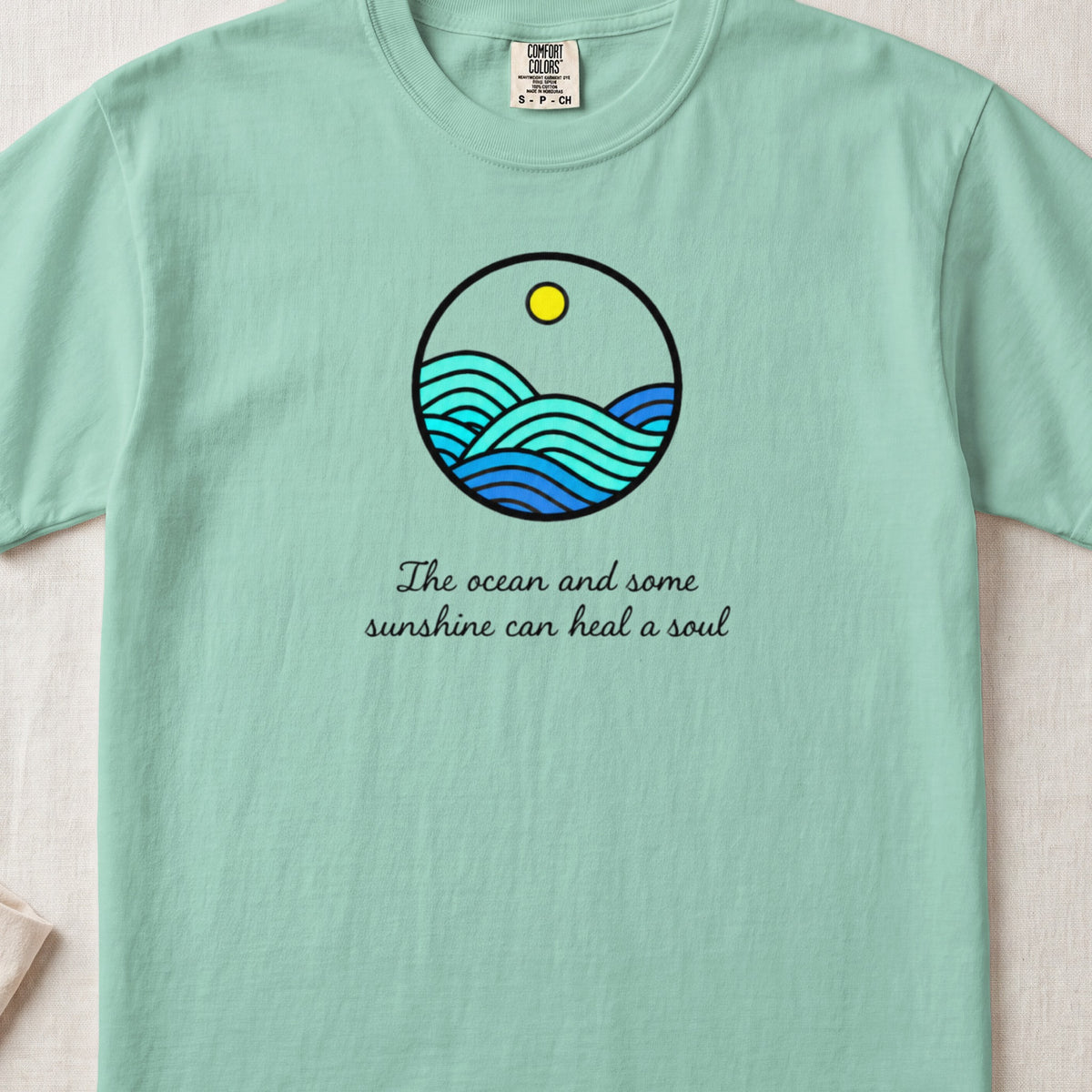 Mint green t-shirt featuring a circular ocean graphic and the text The ocean and some sunshine can heal a soul.