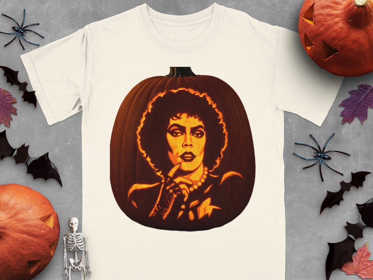A cream-colored t-shirt with a graphic of Frank-N-Furter carved into a glowing pumpkin, surrounded by Halloween decorations.