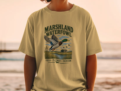 Marshland Waterfowl graphic with flying duck and cabin on a tan t-shirt.