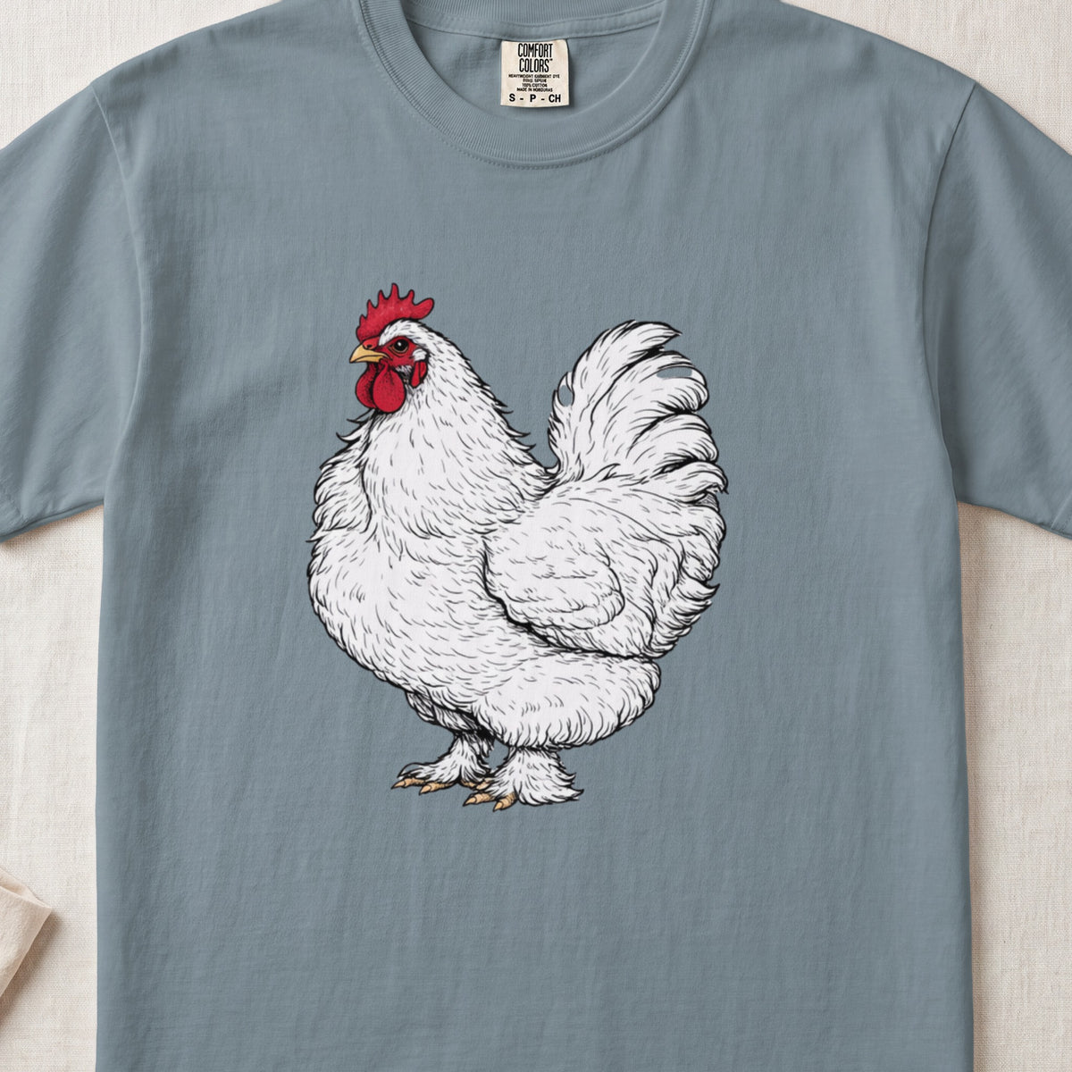 A slate blue t-shirt printed with a detailed sketch of a white rooster with a red comb.