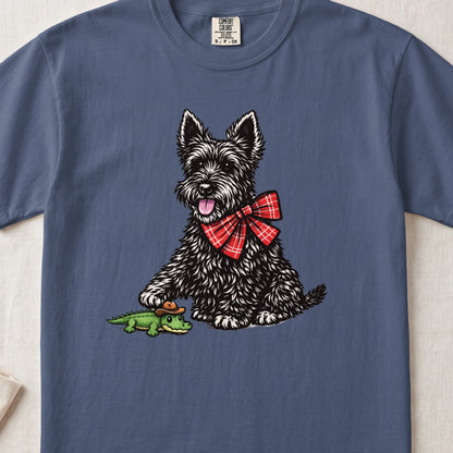 Blue crewneck t-shirt featuring a black Scottish Terrier wearing a red plaid bow tie and playing with a toy alligator.