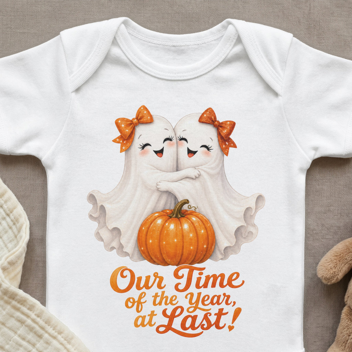 White baby onesie with two hugging ghosts, a pumpkin, and orange text.