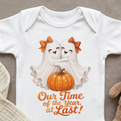 White baby onesie with two hugging ghosts, a pumpkin, and orange text.