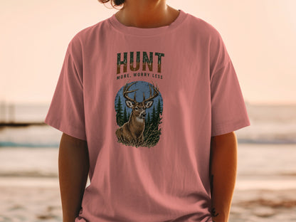 Pink t-shirt with deer and forest graphic, says "HUNT MORE, WORRY LESS".