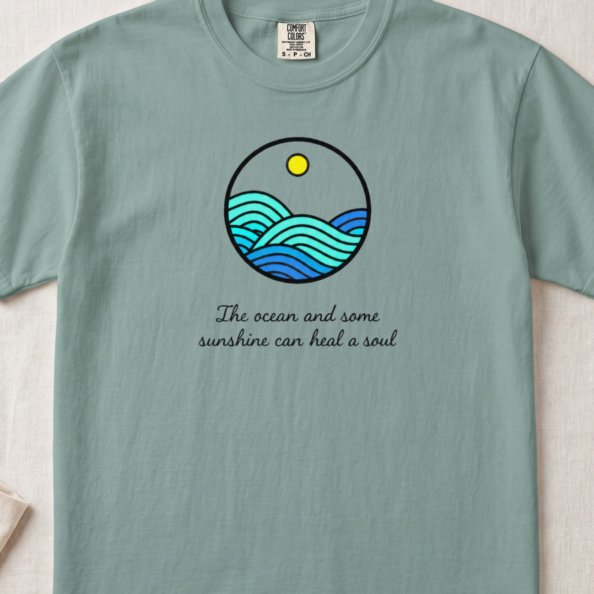 Teal t-shirt with circular ocean waves graphic and text "The ocean and some sunshine can heal a soul."
