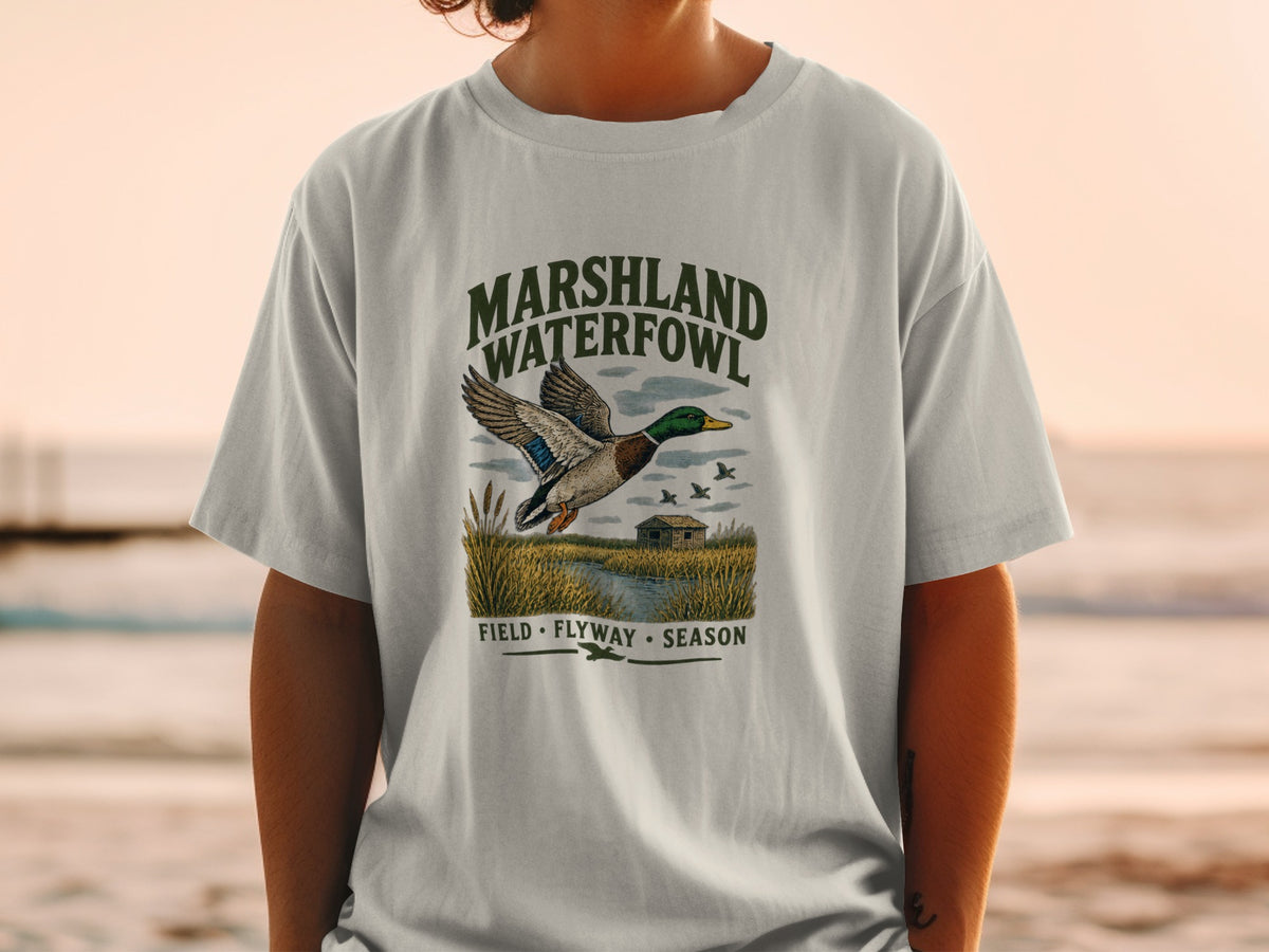 T-shirt graphic with mallard duck flying over marshland, "Marshland Waterfowl" text.