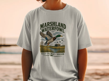 T-shirt graphic with mallard duck flying over marshland, "Marshland Waterfowl" text.