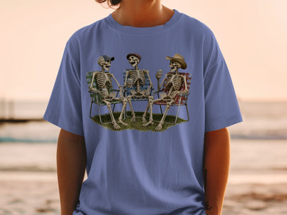 Three skeletons sitting in chairs on grass, wearing hats and holding drinks.