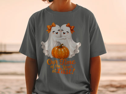 Two ghosts hug a pumpkin on a t-shirt with the text "Our Time of the Year at Last!".