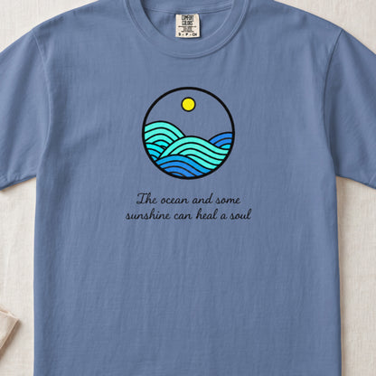 A blue crewneck t-shirt featuring a circular ocean graphic and the text The ocean and some sunshine can heal a soul.