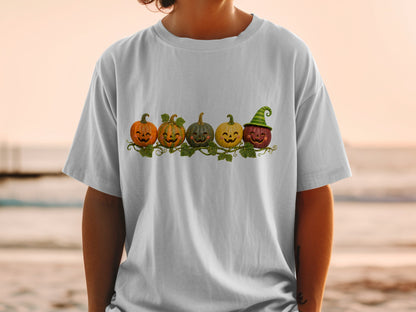 Five cartoon pumpkins with faces, one wearing a witch hat, on a white t-shirt.