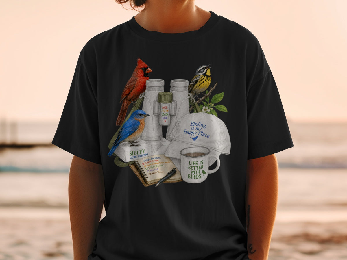 A person wearing a black t-shirt printed with a birdwatching graphic featuring binoculars, birds, and books.
