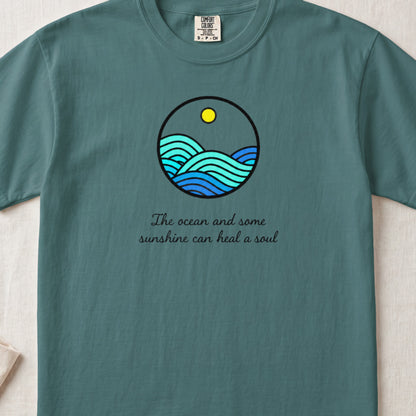 Teal t-shirt featuring a circular graphic of blue ocean waves under a yellow sun, with the text The ocean and some sunshine can heal a soul.