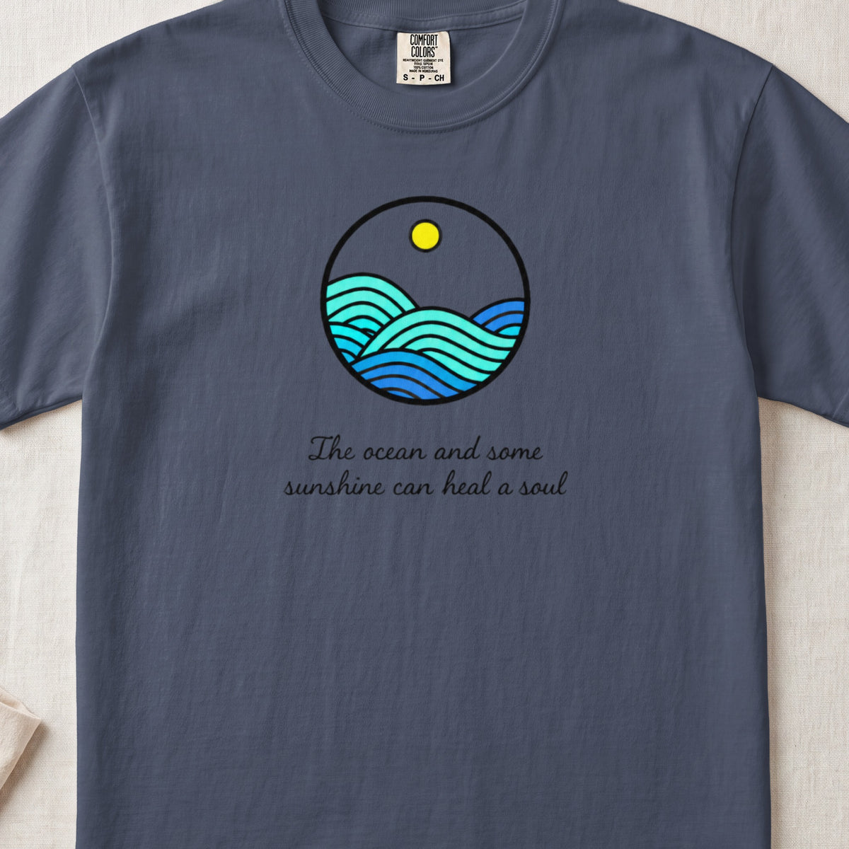 Blue t-shirt with circular ocean wave graphic and "The ocean and some sunshine can heal a soul" text.