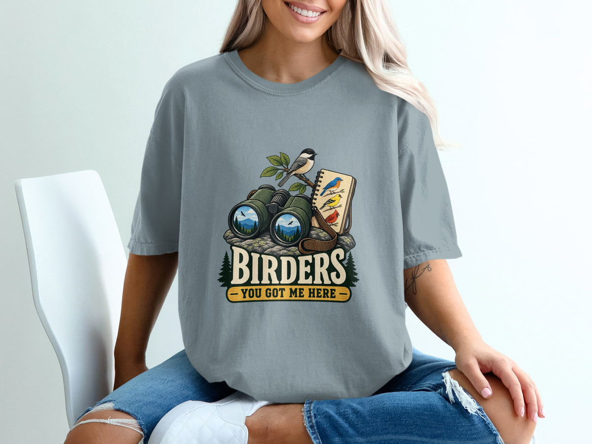 Binoculars, notebook with birds, and text "BIRDERS YOU GOT ME HERE" graphic on t-shirt.