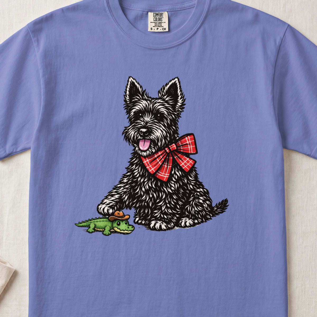 Periwinkle crewneck t-shirt featuring a black Scottish Terrier wearing a red plaid bow tie and touching a toy alligator.