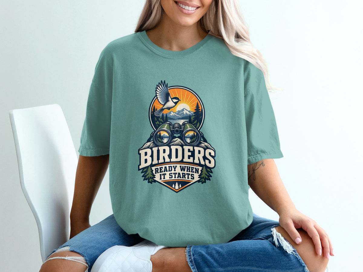 Teal t-shirt with graphic of binoculars, bird, mountains, and text "Birders Ready When It Starts".