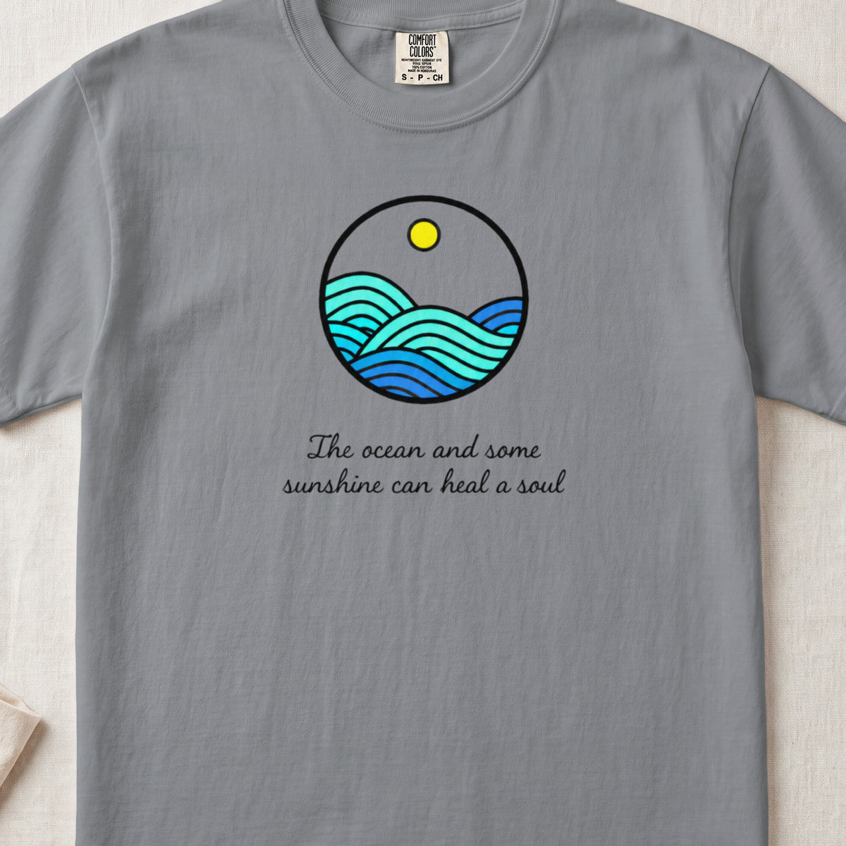 A grey t-shirt featuring a circular ocean graphic and the text The ocean and some sunshine can heal a soul.