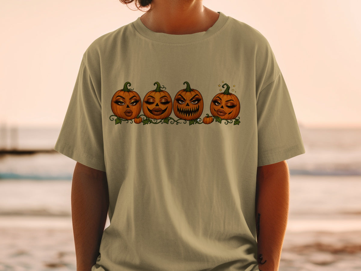 Four cartoon pumpkins with dramatic makeup and expressive faces on a light-colored t-shirt.