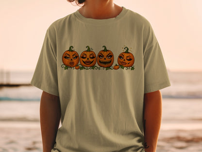 Four cartoon pumpkins with dramatic makeup and expressive faces on a light-colored t-shirt.