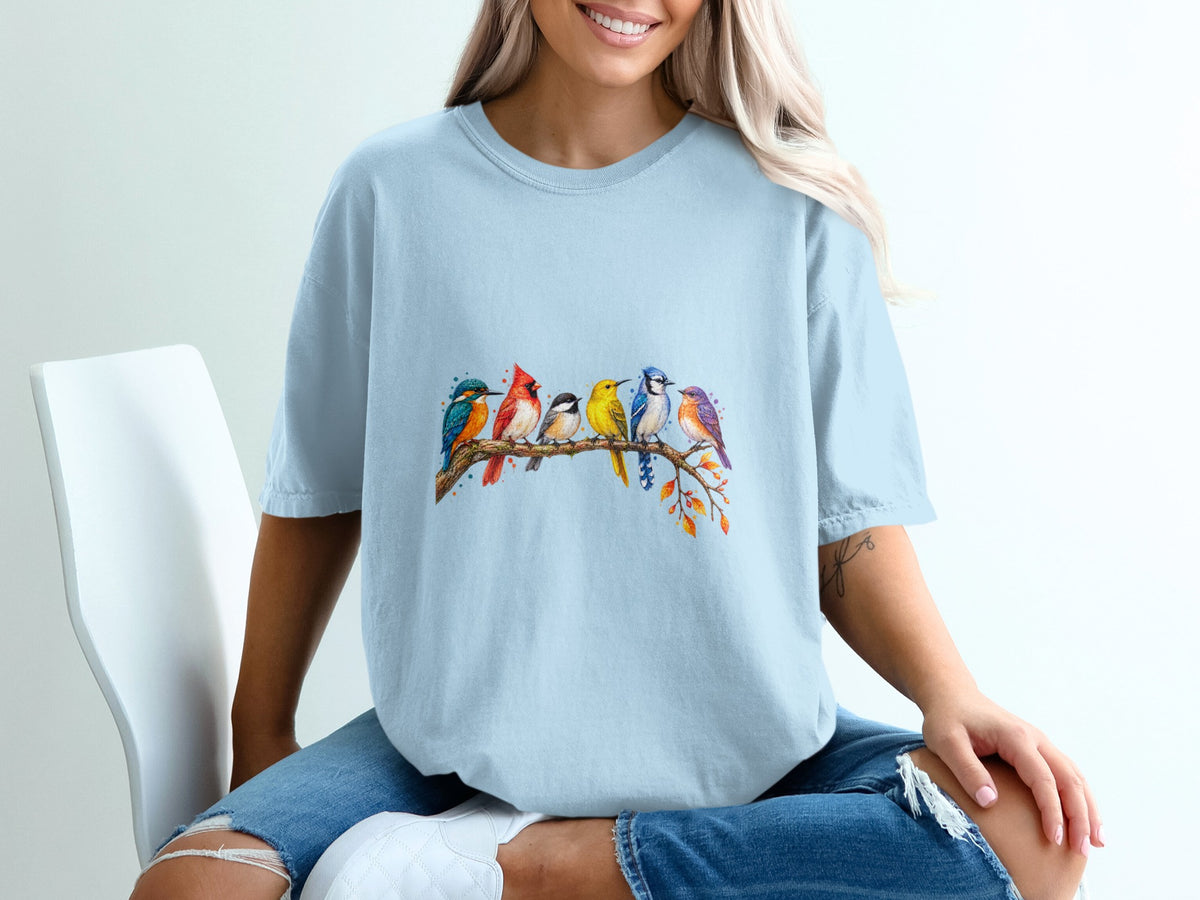 Light blue t-shirt featuring a watercolor illustration of seven colorful birds perched on a branch.