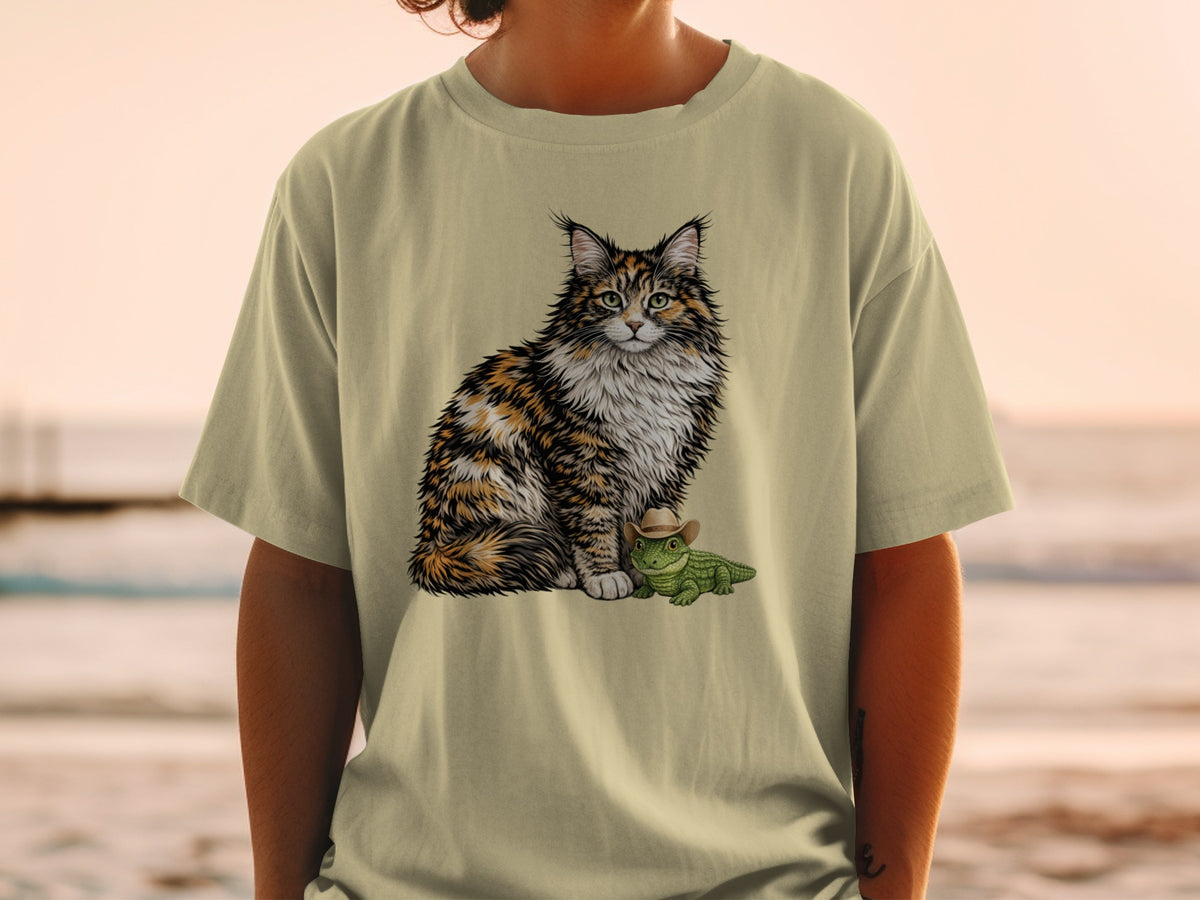 A light-colored t-shirt with a graphic of a fluffy calico cat sitting beside a small alligator wearing a cowboy hat.