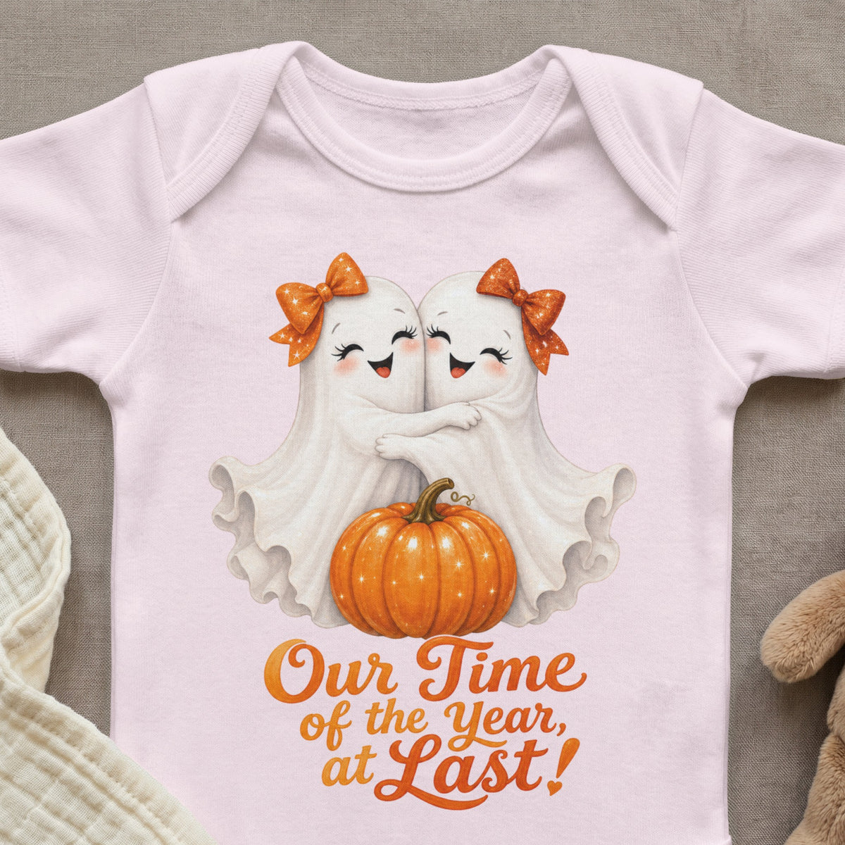 Two white ghosts hugging with orange bows, next to a pumpkin, with text "Our Time of the Year, at Last!".