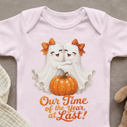 Two white ghosts hugging with orange bows, next to a pumpkin, with text "Our Time of the Year, at Last!".