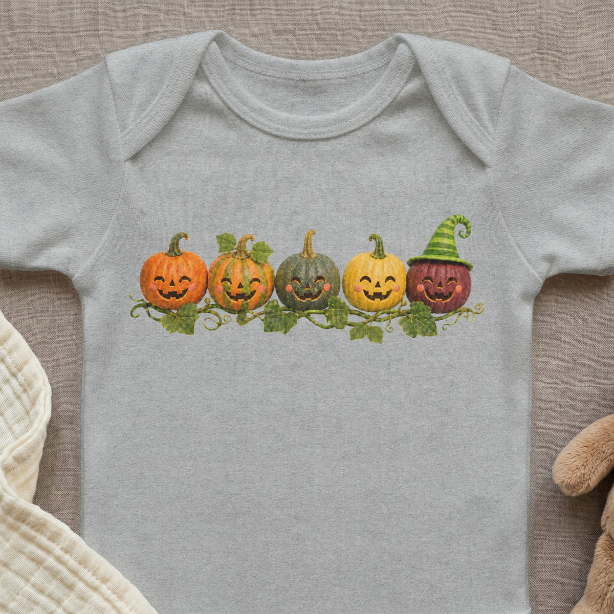 Five smiling cartoon pumpkins with vines and leaves on a grey baby bodysuit.