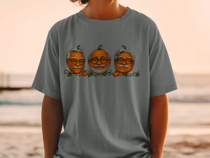 Three pumpkins with human faces and glasses are displayed on a dark grey t-shirt.