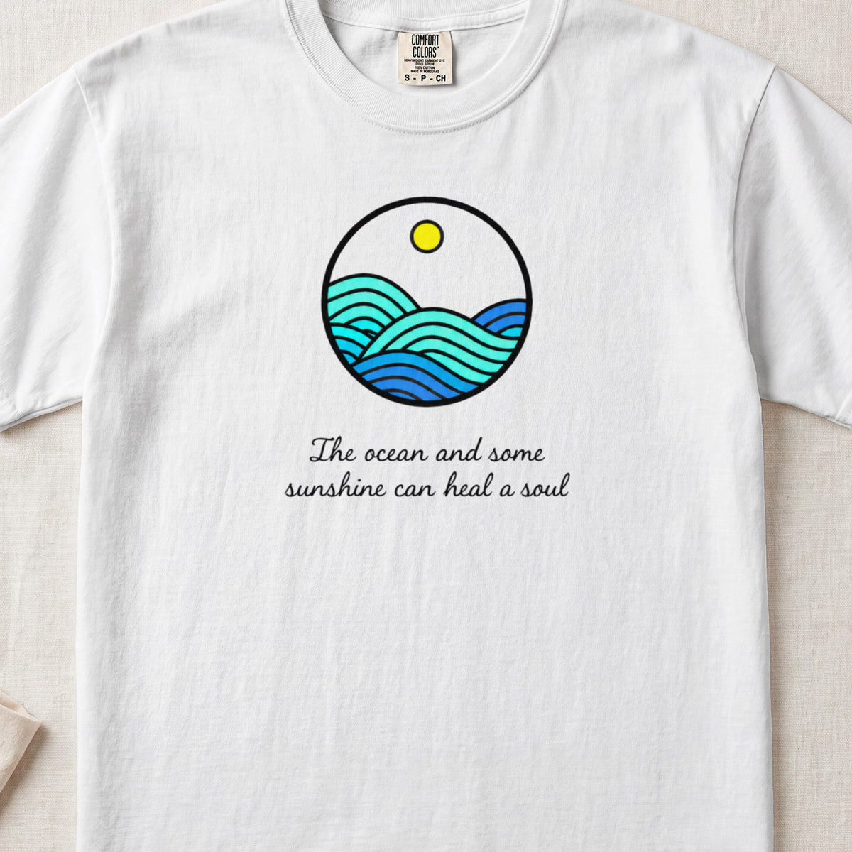 White t-shirt featuring a circular ocean graphic with a yellow sun and handwritten text below.