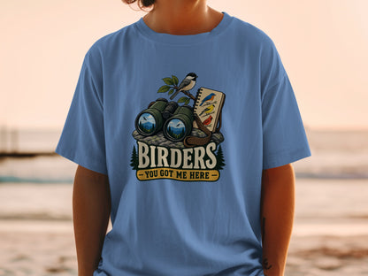Binoculars, birds, and a notebook on a rock with text "BIRDERS YOU GOT ME HERE".