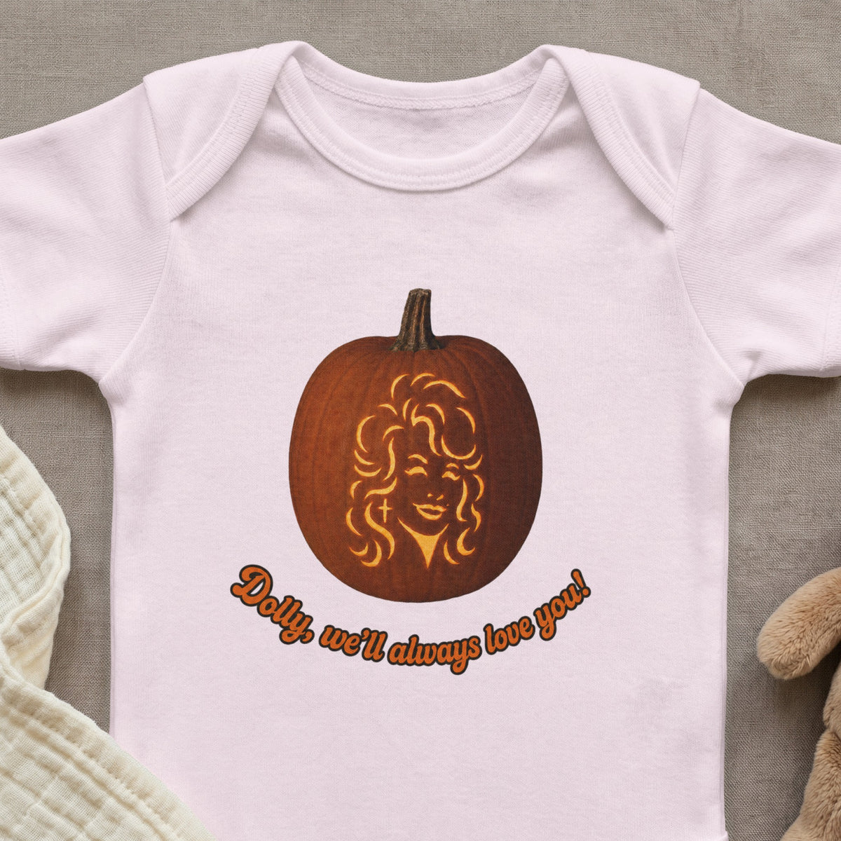 Baby onesie with a carved pumpkin featuring Dolly Parton and text "Dolly, we'll always love you!".