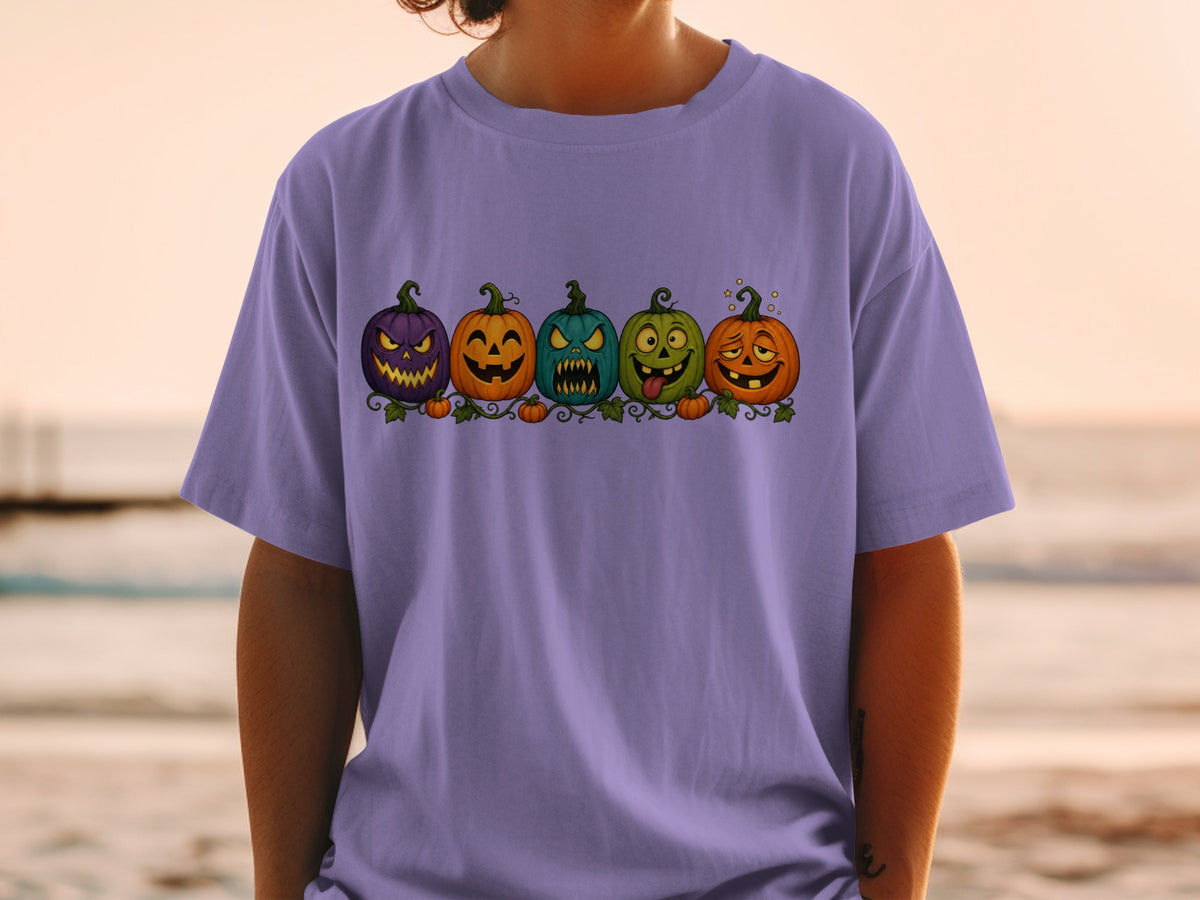 Five cartoon Halloween pumpkins with expressive faces on a purple t-shirt.