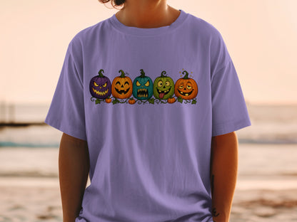 Five cartoon Halloween pumpkins with expressive faces on a purple t-shirt.