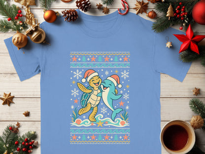 Light blue t-shirt with a cartoon turtle and dolphin wearing Santa hats, surrounded by snowflakes and ocean elements.