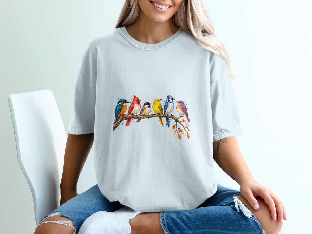 Watercolor print of seven colorful birds perched on a branch on a light gray t-shirt.