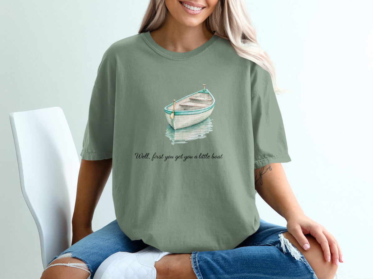 Green t-shirt with watercolor painting of a rowboat and the text "Well, first you get you a little boat".