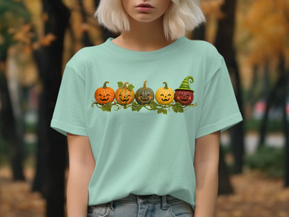 Five smiling cartoon pumpkins with vines and leaves on a light teal t-shirt.