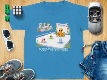 Blue t-shirt with "Ocean Olympics" text and cartoon sea creatures playing water polo.