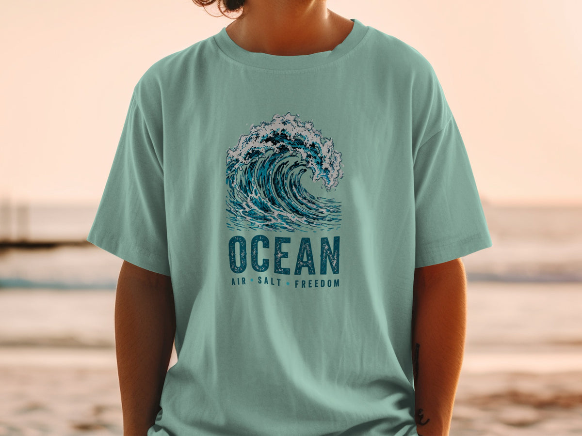 Teal t-shirt with crashing wave graphic and text "OCEAN AIR SALT FREEDOM."