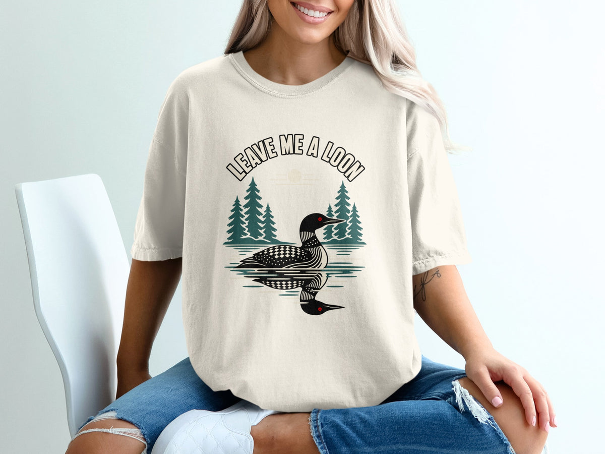 Cream t-shirt with graphic of loon on water, trees, and text "LEAVE ME A LOON".