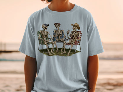 Three skeletons in lawn chairs holding drinks with a sunset beach background.
