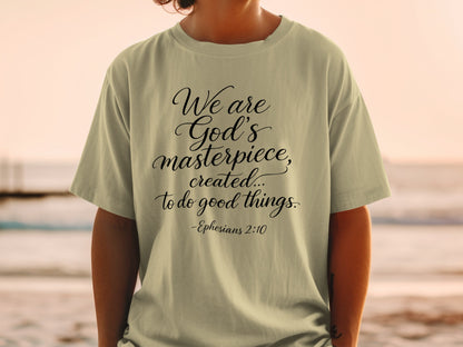 Light tan t-shirt with black cursive text reading "We are God's masterpiece, created... to do good things. -Ephesians 2:10"