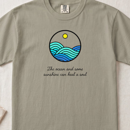 Sage green t-shirt featuring a circular ocean graphic with a sun and the text The ocean and some sunshine can heal a soul.