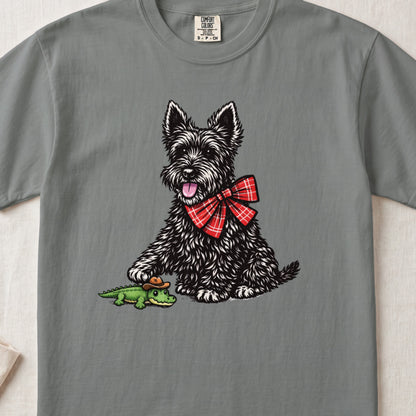 Grey t-shirt featuring an illustration of a black terrier wearing a red plaid bow tie and touching a toy alligator.